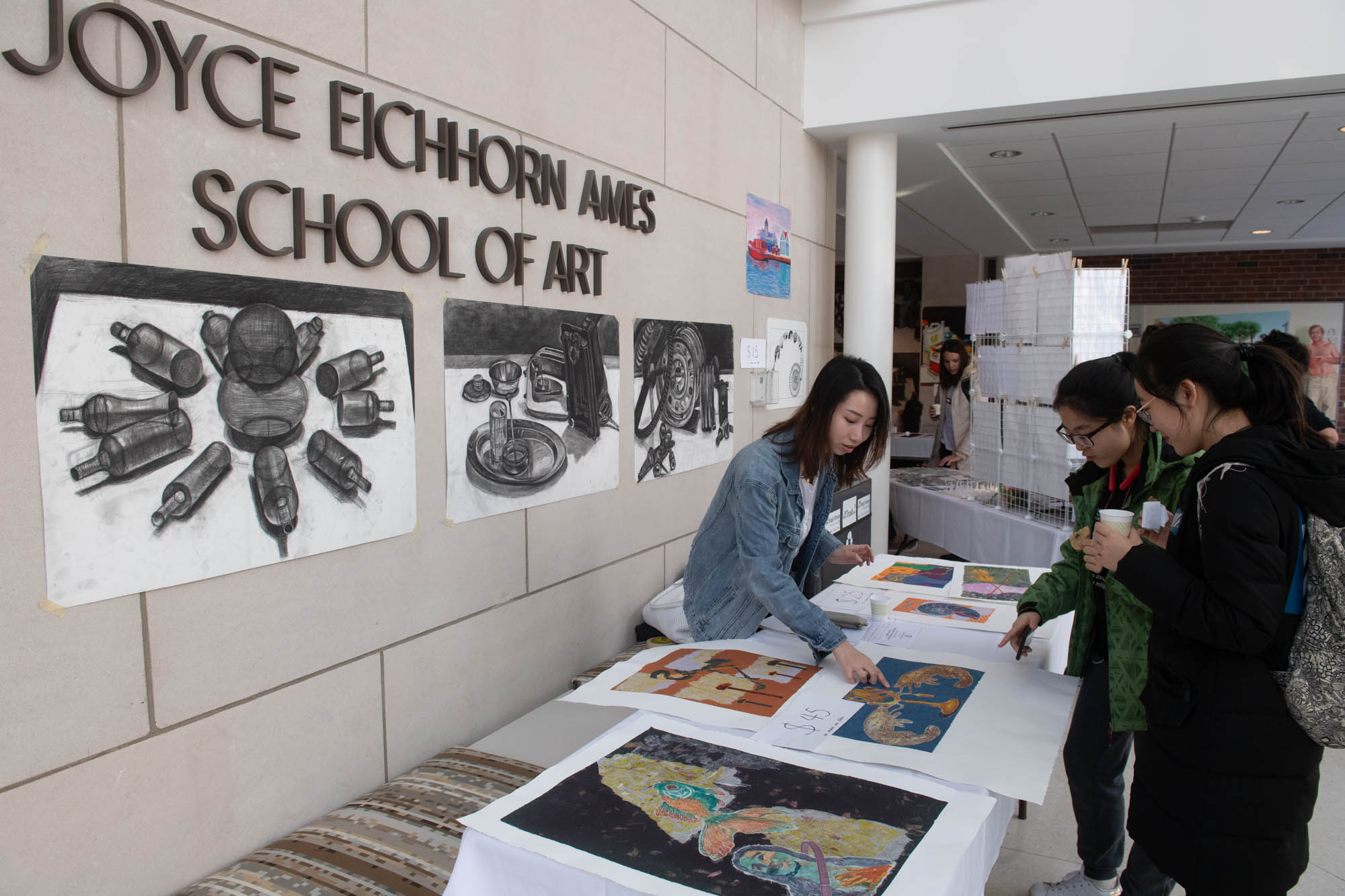 Student artist pointing at art print in front of Joyce Eichhorn Ames School of Art and Design sign