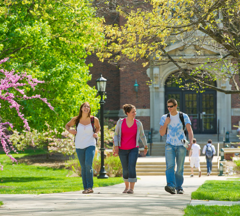 Students walk on the quad in front of Presser Hall with flowers