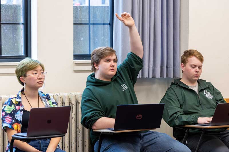 Students in a classroom with one student raising their hand.