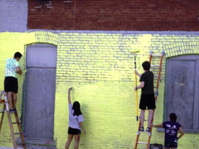 Students paint a brick wall of West Bloomington Revitalization Project in preparation for a mural