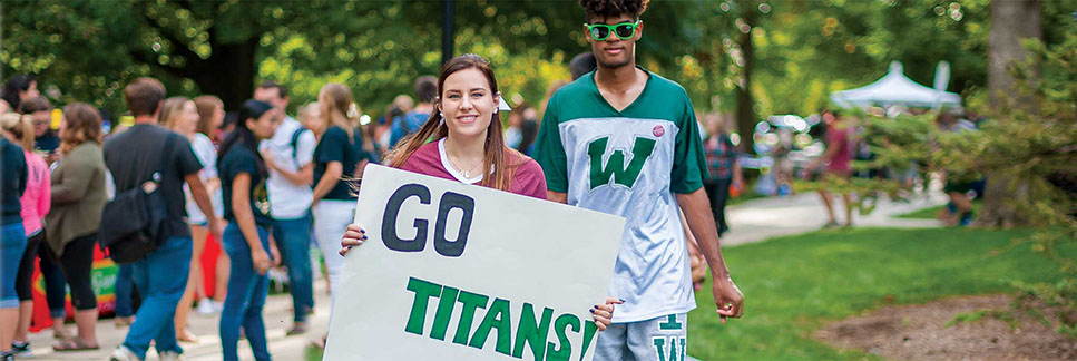 Student smiling and holding "Go Titans!" sign