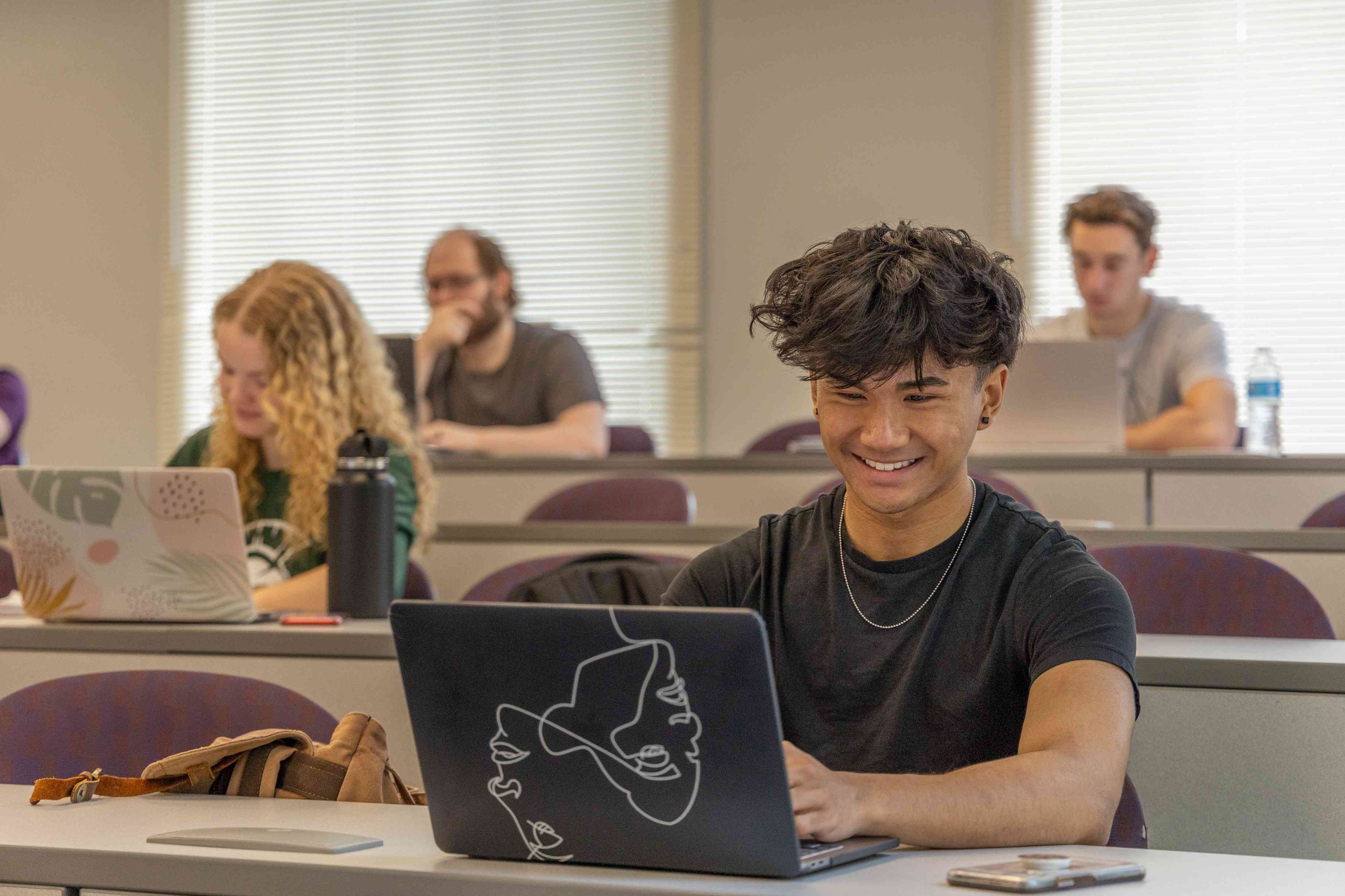 Male student smiles while working on his laptop in a classroom