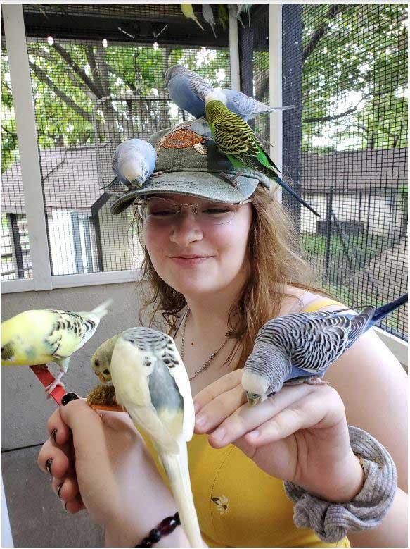 Several birds perch on Lizzie Baranski as she smiles.