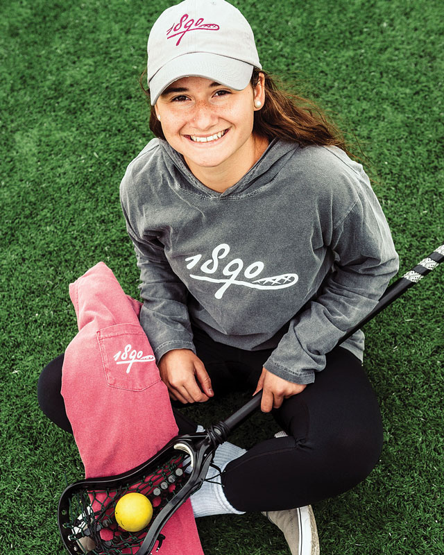 Claudia Richman '19 smiles while holding lacrosse gear and 1890 branded clothing and accessories