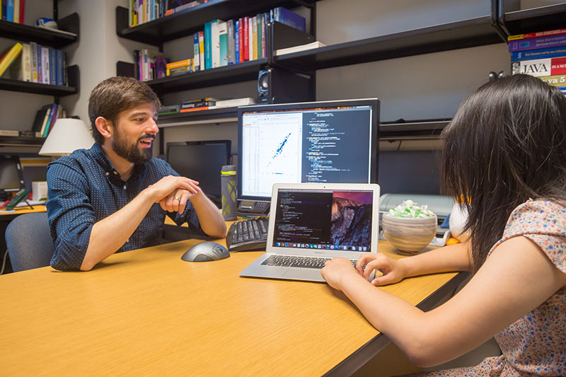 Professor and student facing computer, discussing research.