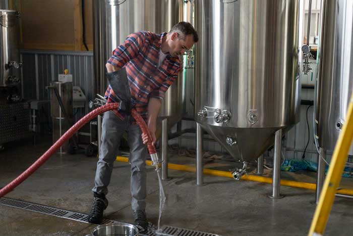Ryan Reber uses a hose to sterilize a component of the fermentation tanks.