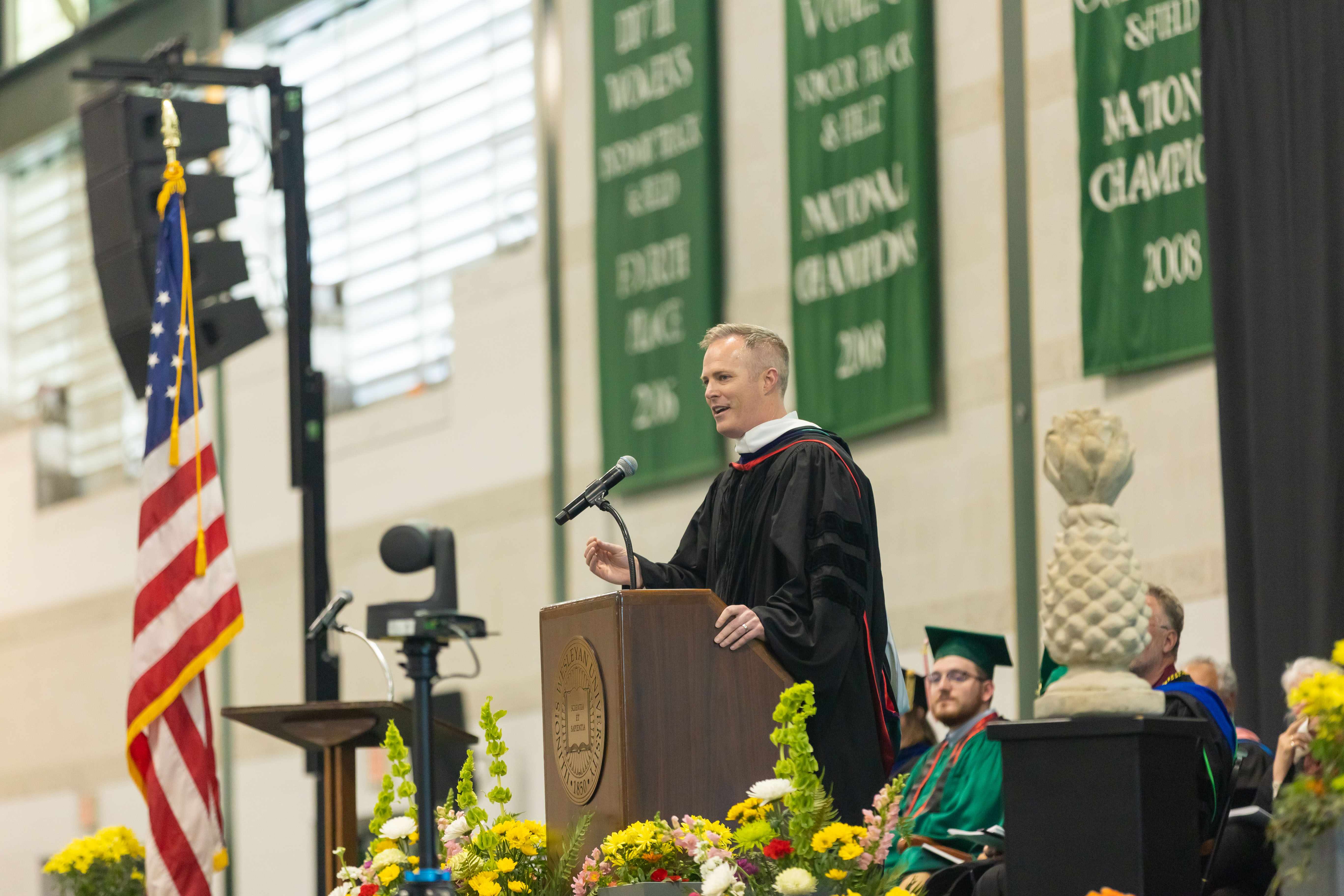 Burke Nihill speaking at podium during Illinois Wesleyan commencement ceremony