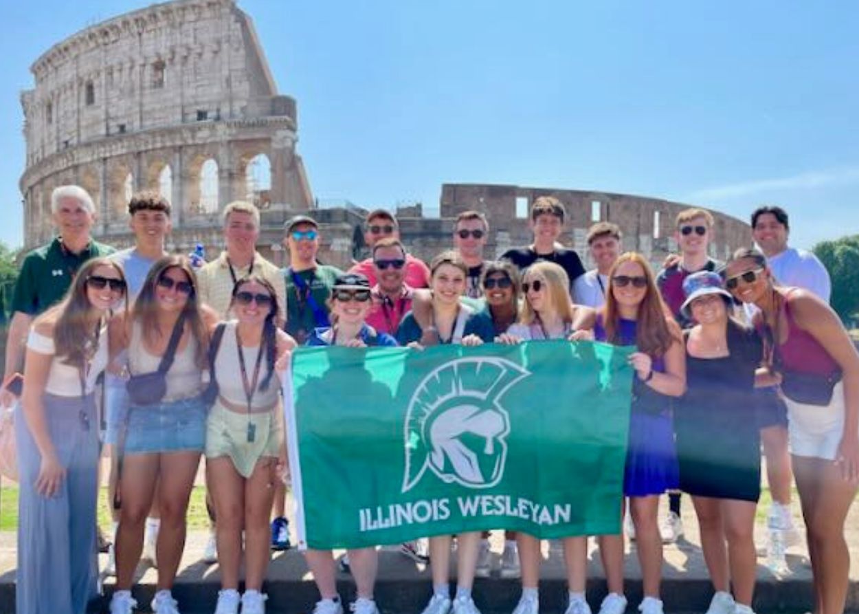 Students hold IWU flag against backdrop pof the Colosseum