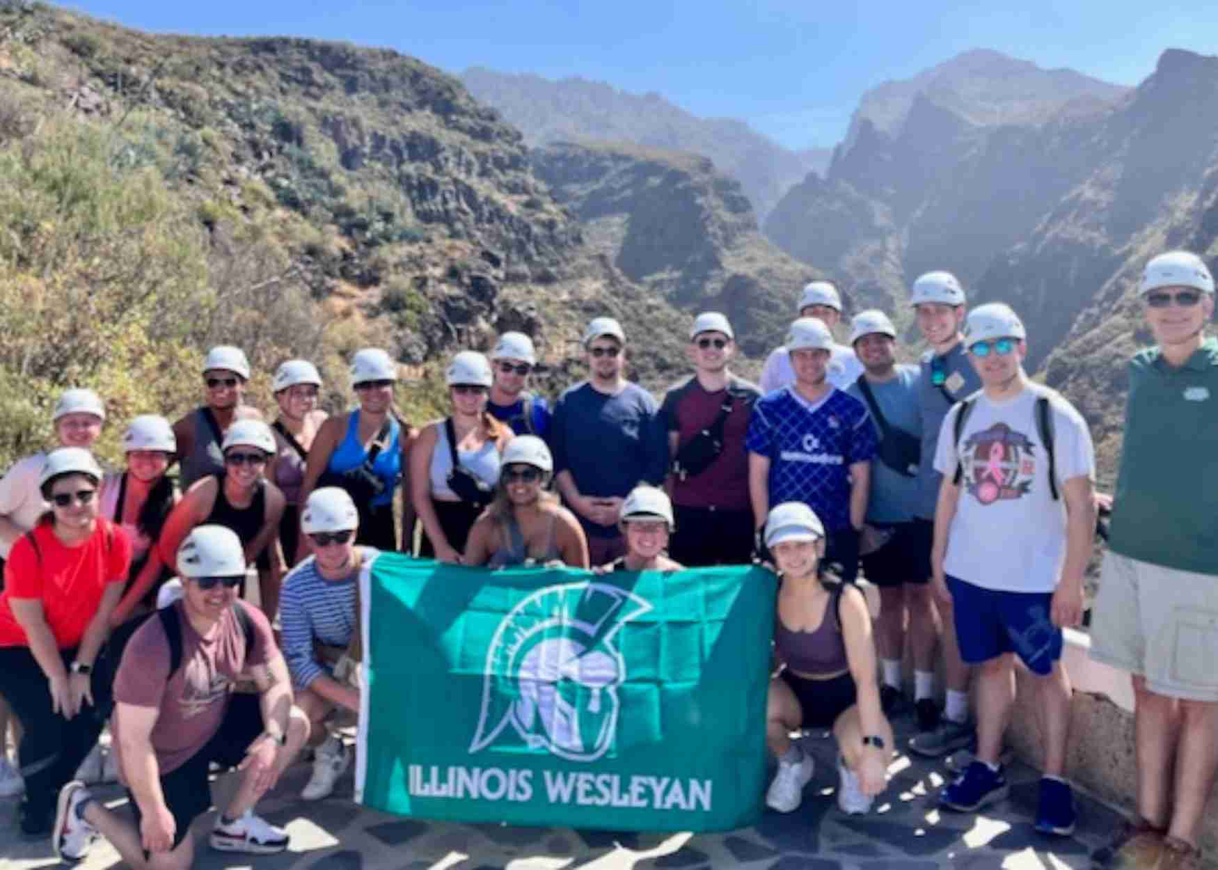 Group of students hold IWU flag against mountain backdrop during travel seminar visit to Canary Islands