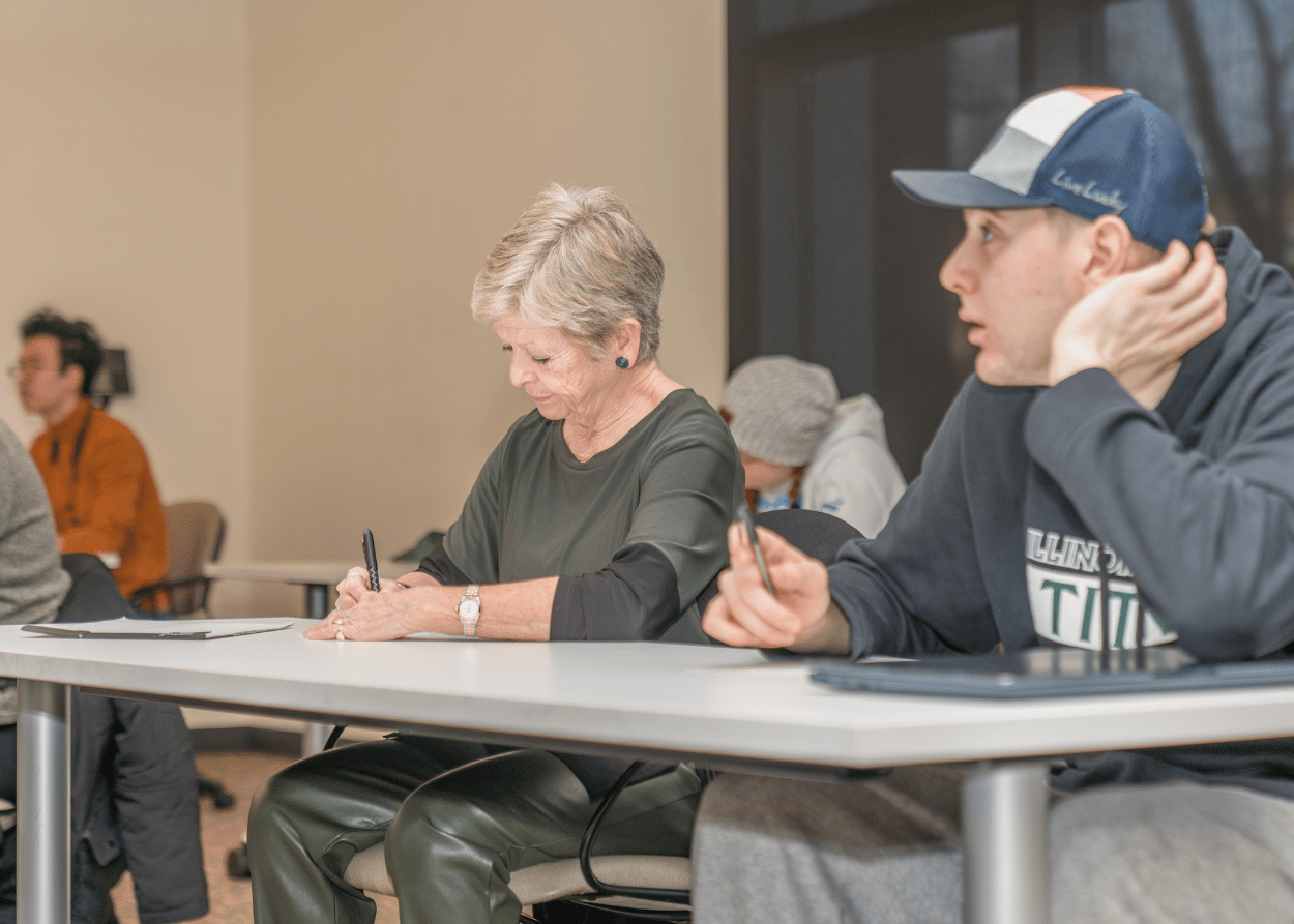 President Nugent sits in classroom taking notes with other students