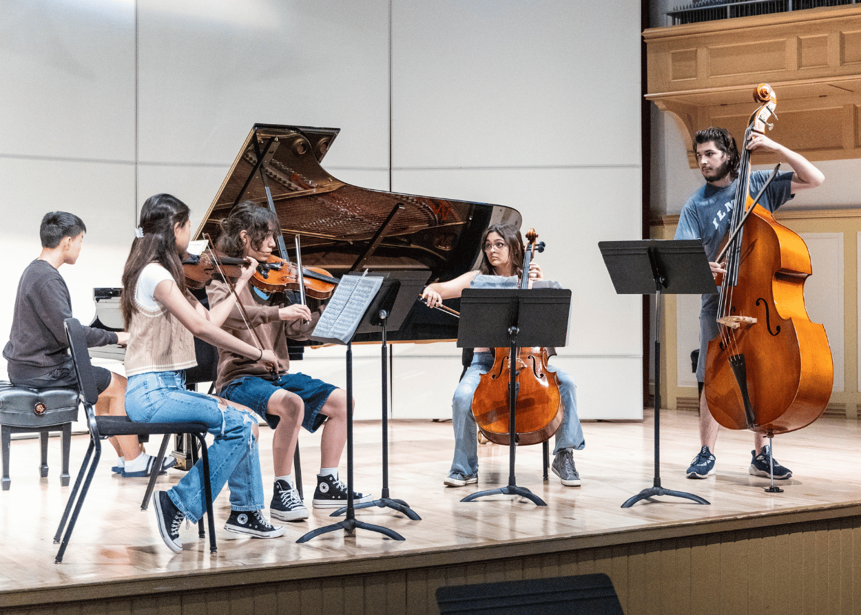 Students perform string instruments on stage at Westbrook Auditorium
