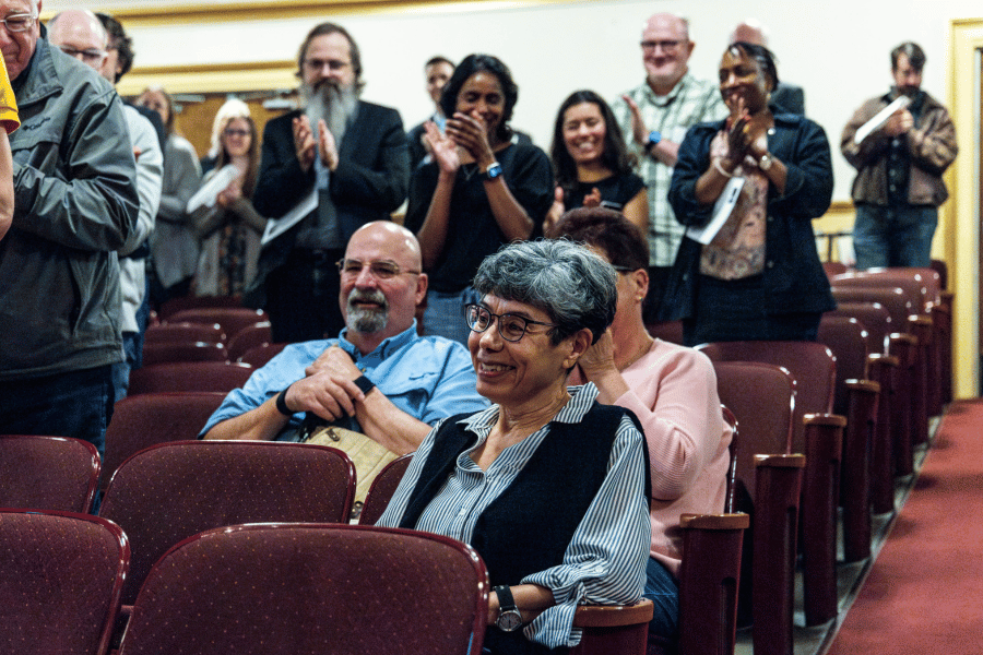 Zahia Drici seated in auditorium as audience stands and applauds around her