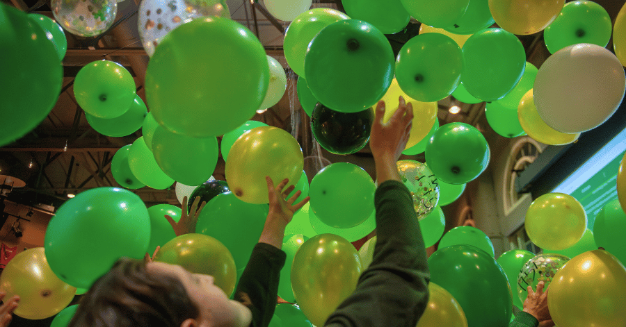 Student lifting hands to green balloons falling from the ceiling of Hansen Student Center