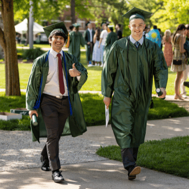Students walking on IWU quad in cap and gown after grauation, one giving thumbs up