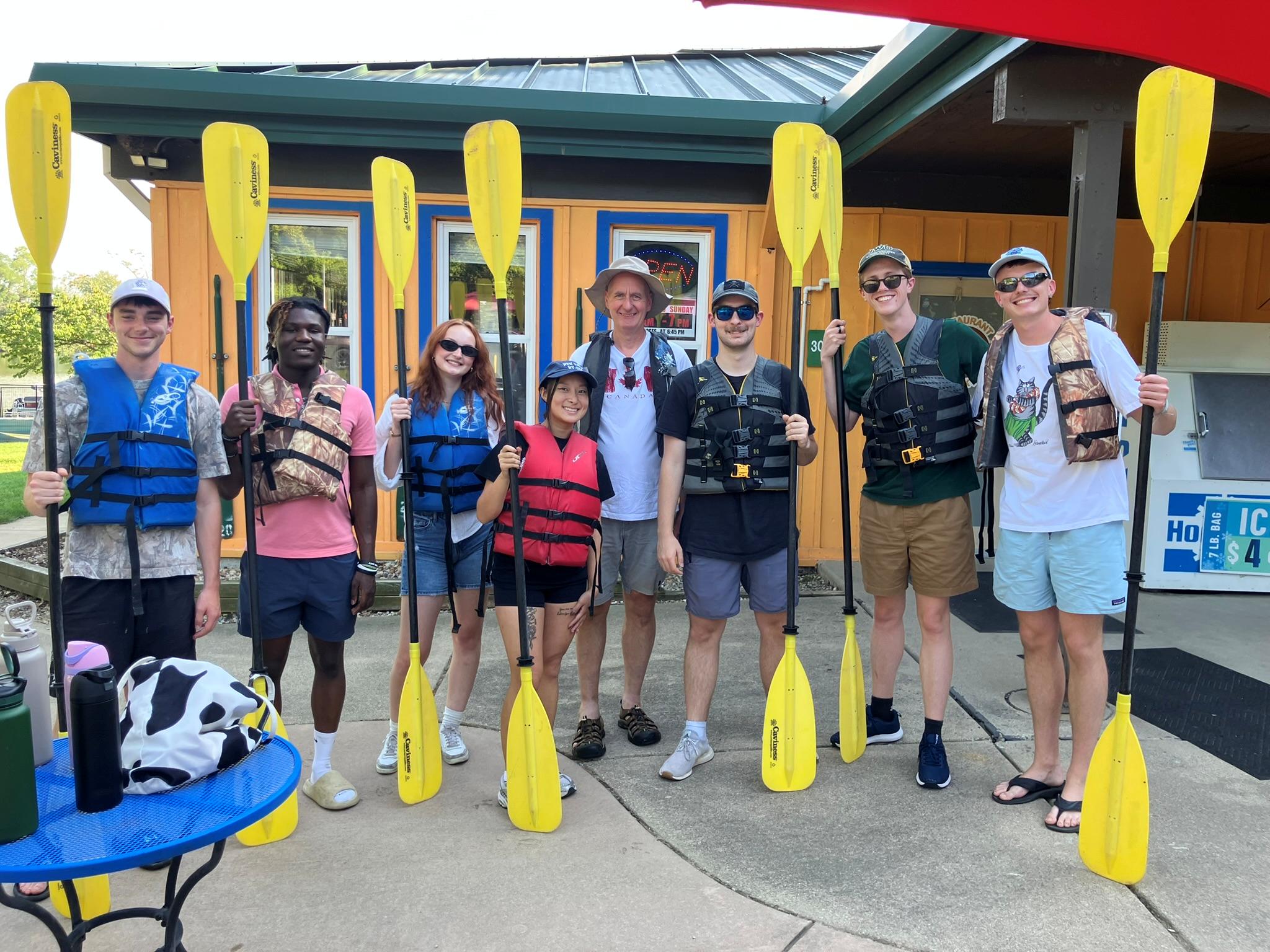 Students and faculty standing with kayak paddles